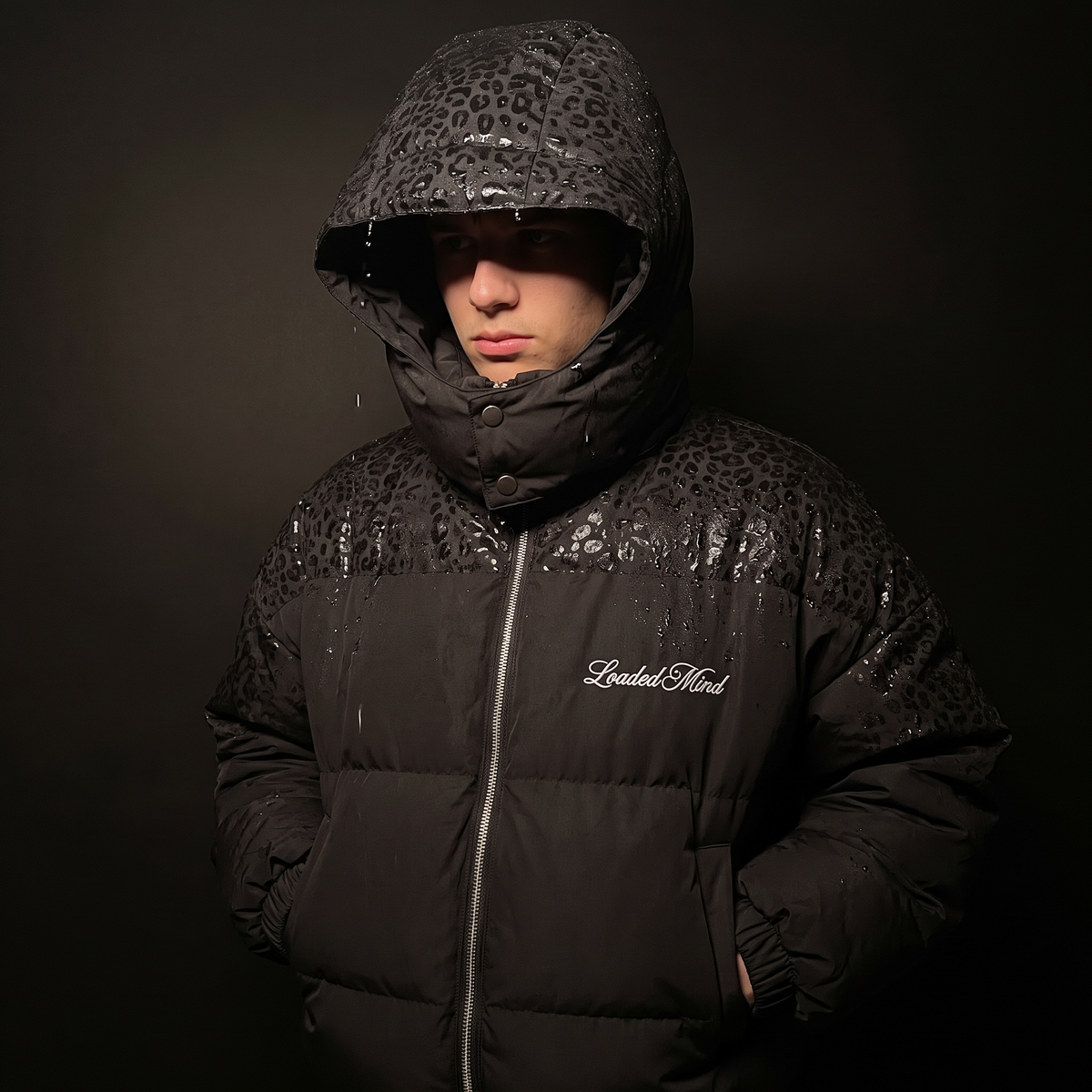 Black leopard reveal puffer on a man, hood up and soaked, pattern showing